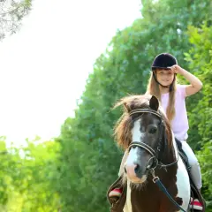 Uśmiechnięta dziewczynka w kasku na koniu. Radosna jazda konna dla dzieci wśród zieleni.
