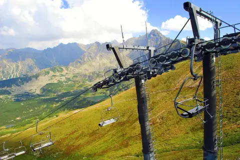 Wyciąg krzesełkowy Zakopane wita w Tatrach. Puste krzesełka wiszą na tle gór i zielonych zboczy.